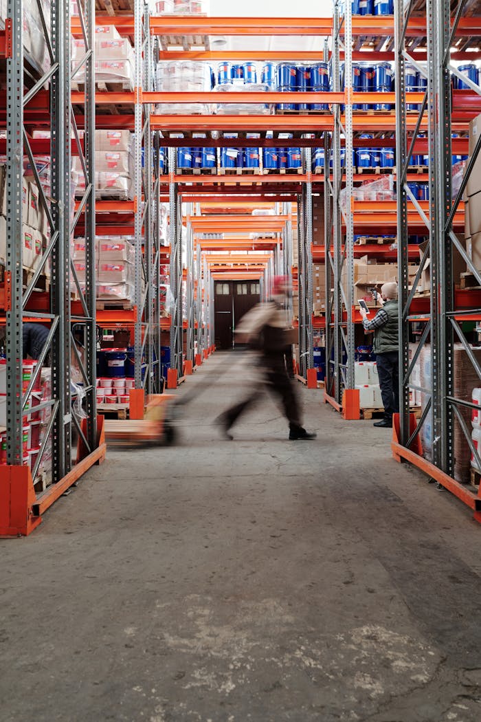 services-03 Blurred motion of a man walking in a spacious warehouse aisle between tall shelves.